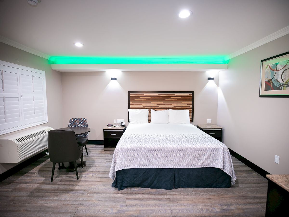 A well-lit hotel room with a bed, two nightstands, a desk and chair, a window with white shutters, and modern decor with a framed picture on the wall.