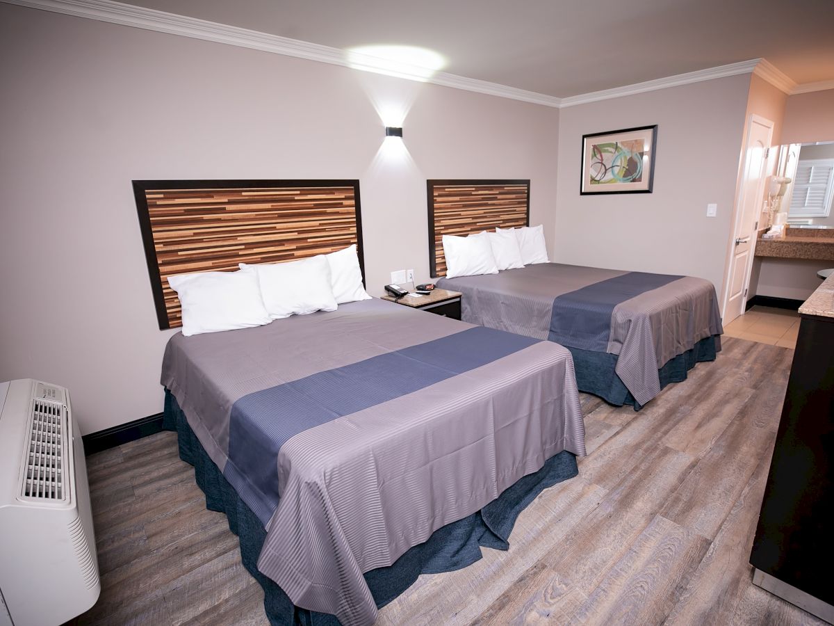 This image shows a hotel room with two double beds, a wall lamp, an air conditioner, a picture frame, and a partial view of a bathroom.