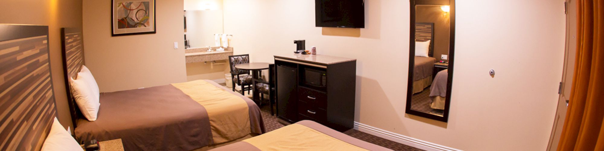 The image shows a hotel room with two beds, a TV, a mirror, a desk with a chair, a coffee maker, and a bathroom area in the background.